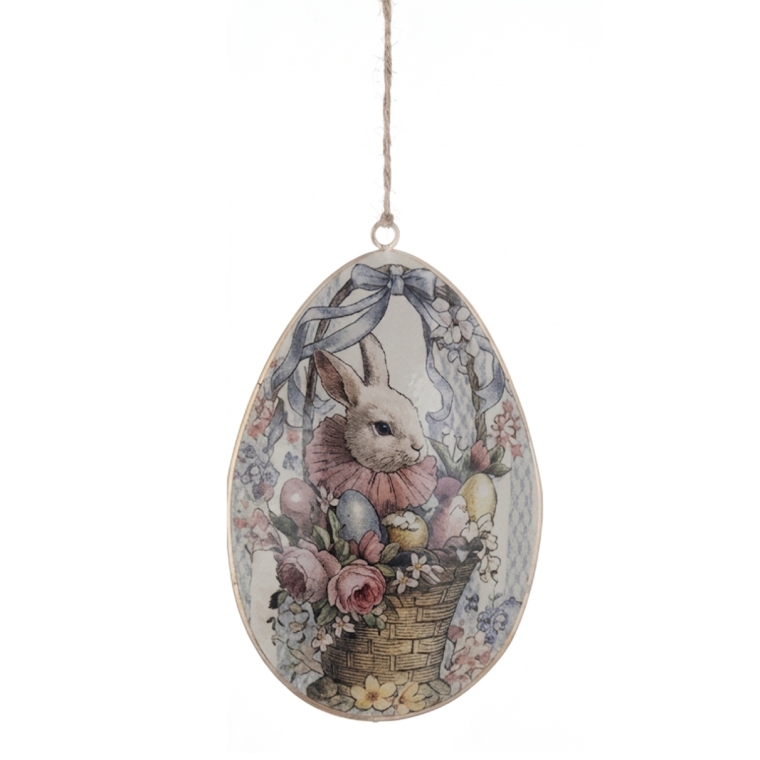 Pendaglio pasquale a forma di uovo in metallo della collezione "Joyeuses Paques" di Blanc Mariclo'. La decorazione presenta un disegno d'ispirazione retrò con un tenero coniglio che spunta da un cesto intrecciato ricolmo di uova colorate, rose e fiori nei toni del rosa e dell'azzurro, ideale per addobbi pasquali in stile country chic.