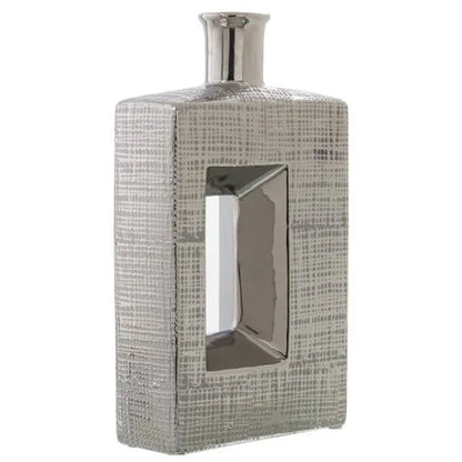 Vaso a bottiglia rettangolare verticale firmato Camacho, caratterizzato da un'elegante finitura ceramica color argento lucido con una texture a rilievo finemente lavorata e un originale design geometrico con foro centrale vuoto. Questo moderno complemento d'arredo è provvisto di un collo stretto superiore ideale per ospitare singoli steli floreali, perfetto come sofisticato oggetto ornamentale per impreziosire mobili, consolle o tavoli in contesti contemporanei.