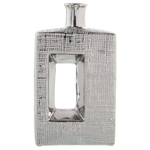 Vaso a bottiglia rettangolare verticale firmato Camacho, caratterizzato da un'elegante finitura ceramica color argento lucido con una texture a rilievo finemente lavorata e un originale design geometrico con foro centrale vuoto. Questo moderno complemento d'arredo è provvisto di un collo stretto superiore ideale per ospitare singoli steli floreali, perfetto come sofisticato oggetto ornamentale per impreziosire mobili, consolle o tavoli in contesti contemporanei.