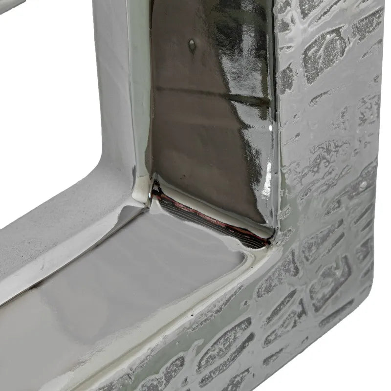 Vaso a bottiglia rettangolare orizzontale firmato Camacho, caratterizzato da un'elegante finitura ceramica color argento lucido con una texture a rilievo finemente lavorata e un originale design geometrico irregolare con foro centrale vuoto. Questo moderno complemento d'arredo è provvisto di un collo stretto superiore ideale per ospitare singoli steli floreali, perfetto come sofisticato oggetto ornamentale per impreziosire mobili, consolle o tavoli in contesti contemporanei.