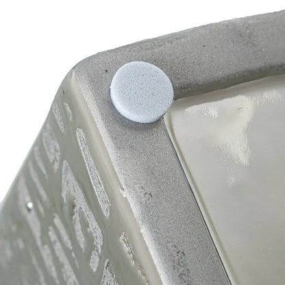 Vaso a bottiglia rettangolare orizzontale firmato Camacho, caratterizzato da un'elegante finitura ceramica color argento lucido con una texture a rilievo finemente lavorata e un originale design geometrico irregolare con foro centrale vuoto. Questo moderno complemento d'arredo è provvisto di un collo stretto superiore ideale per ospitare singoli steli floreali, perfetto come sofisticato oggetto ornamentale per impreziosire mobili, consolle o tavoli in contesti contemporanei.