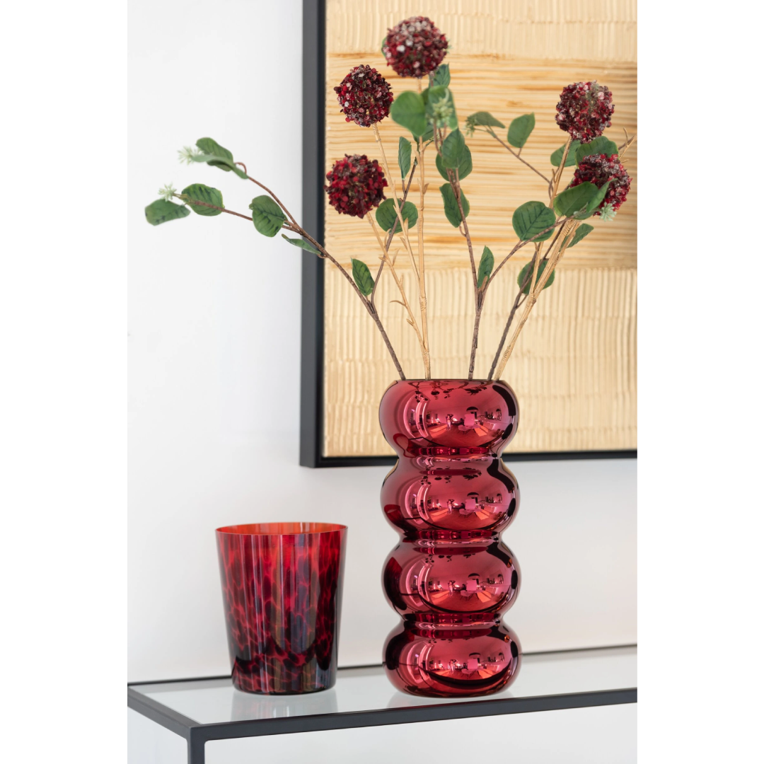 Vaso in vetro rosso scuro modello Bruco firmato Jolipa, caratterizzato da un design moderno e sinuoso a sezioni sferiche sovrapposte con finitura lucida e metallizzata. Questo originale vaso decorativo di design è perfetto come centrotavola o portafiori elegante per arredare con uno stile ricercato e contemporaneo gli interni della casa.