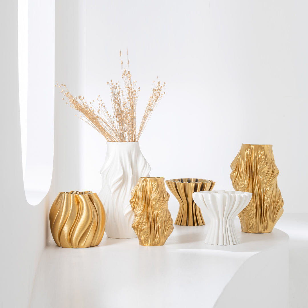 Composizione di vasi in porcellana della collezione 3D in vari formati, colori oro e bianco opaco. I vasi presentano forme scultoree asimmetriche e texture rigate, disposti su un piano bianco minimalista.