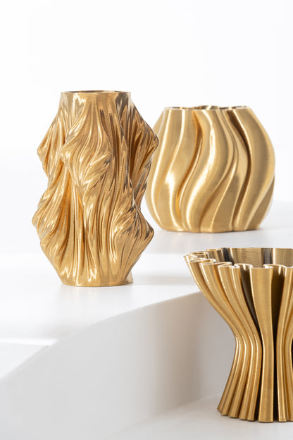 Set di vasi di design in porcellana oro di diverse altezze e forme scultoree. I vasi presentano texture rigate e geometrie irregolari, disposti su due piani bianco moderno.