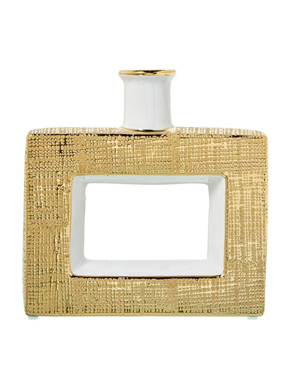 Vaso a bottiglia rettangolare orizzontale firmato Camacho, caratterizzato da un'elegante finitura ceramica color oro lucido con una texture a rilievo finemente lavorata, dettagli bianchi e un originale design geometrico con foro centrale vuoto. Questo moderno complemento d'arredo è provvisto di un collo stretto superiore ideale per ospitare singoli steli floreali, perfetto come sofisticato oggetto ornamentale per impreziosire mobili, consolle o tavoli in contesti contemporanei.