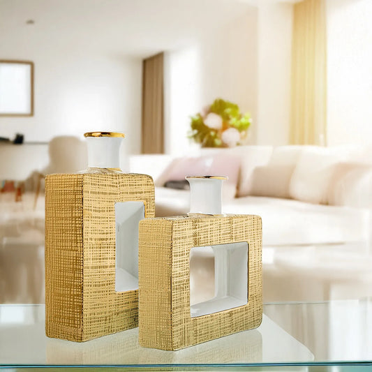 Vaso a bottiglia rettangolare verticale firmato Camacho, caratterizzato da un'elegante finitura ceramica color oro lucido con una texture a rilievo finemente lavorata, dettagli bianchi e un originale design geometrico con foro centrale vuoto. Questo moderno complemento d'arredo è provvisto di un collo stretto superiore ideale per ospitare singoli steli floreali, perfetto come sofisticato oggetto ornamentale per impreziosire mobili, consolle o tavoli in contesti contemporanei.