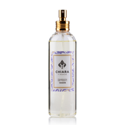 Fragranza spray per tessuti in flacone di vetro trasparente con erogatore dorato, etichetta decorata con motivo botanico a rami e foglie lilla "Venereo" firmata Chiara Firenze. Profumatore per tessuti elegante con logo a giglio, ideale per rinfrescare la casa o come idea regalo raffinata.